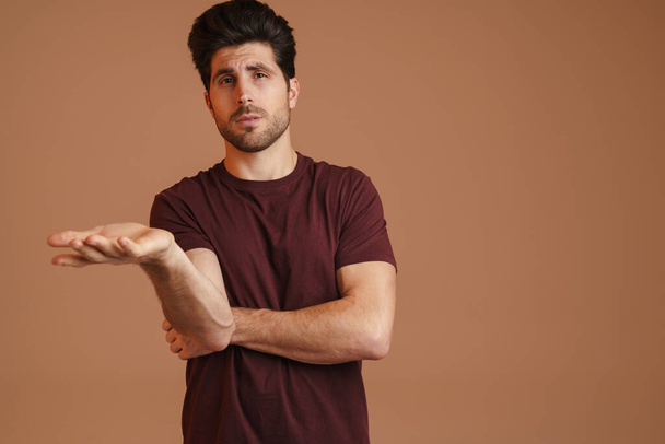 Confused masculine man gesturing and looking at camera isolated over beige background - Фото, зображення