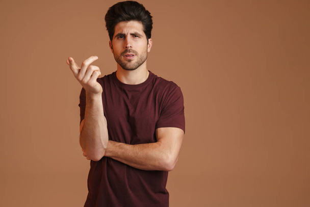 Confused masculine man gesturing and looking at camera isolated over beige background - 写真・画像