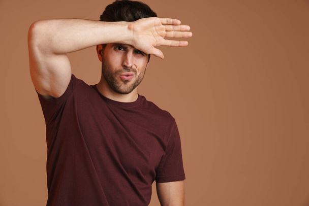 Displeased young man with headache touching his forehead isolated over beige background - Foto, Bild