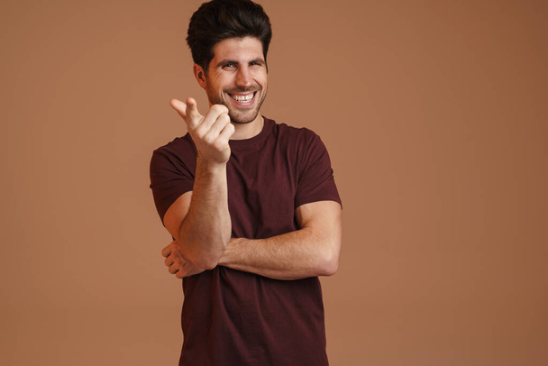 Joyful masculine man smiling and pointing finger at camera isolated over beige background - Foto, afbeelding