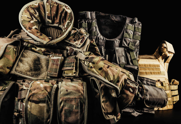 Varios tipos de chalecos blindados camuflados de soldado con protección de hombro y cuello sobre fondo negro tendidos en la mesa. - Foto, imagen