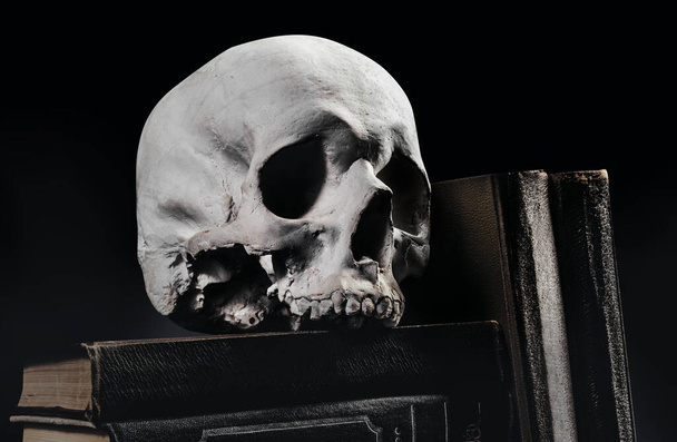 古い本の上に横たわる魔術人の頭蓋骨の写真と黒の背景に積み重ねられた本. - 写真・画像
