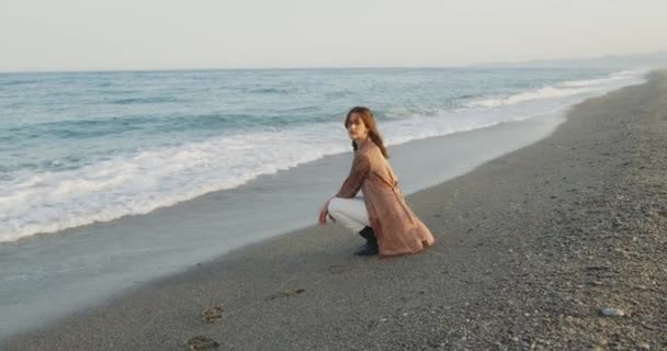 Siyah çizmeleri ve beyaz pantolonu olan güzel bir İtalyan kızı yazın deniz kenarında dinleniyor. - Video, Çekim