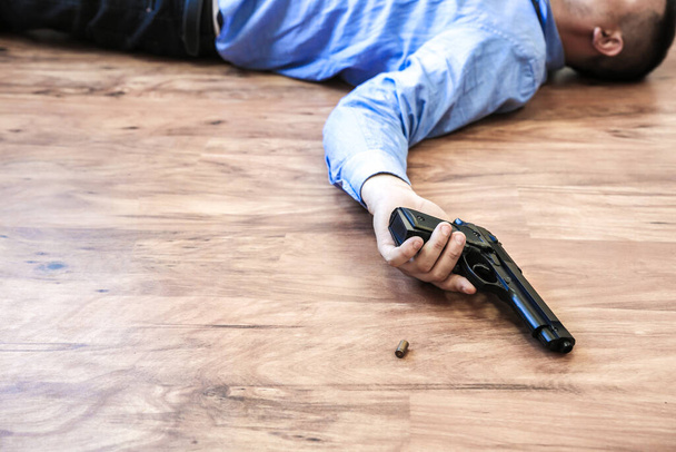 Office worker lies on the floor holding gun in his hands. Suicide because of work stress. Depression or burnout. Terrible life situation. Man near the laptop at the desk. - Photo, Image