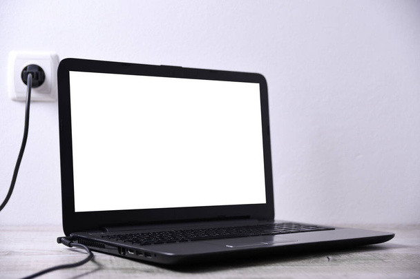 Laptop, de computer laadt op van een 220 volt stopcontact op een bureau vlakbij de muur. Energie, accumulatie - Foto, afbeelding