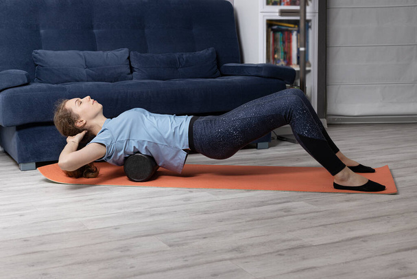 ejercicios para la espalda con un rodillo de gimnasia en la estera. Chica se dedica a estirar en casa en el suelo. - Foto, imagen