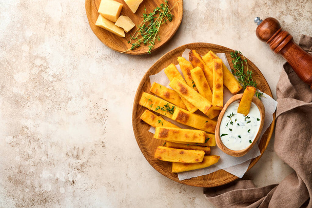 Homemade polenta chips fries with sea salt, parmesan, thyme, rosemary with yogurt sauce. Typical Italian fried polenta. Fried corn sticks. Old light concrete background. Top view - Photo, image