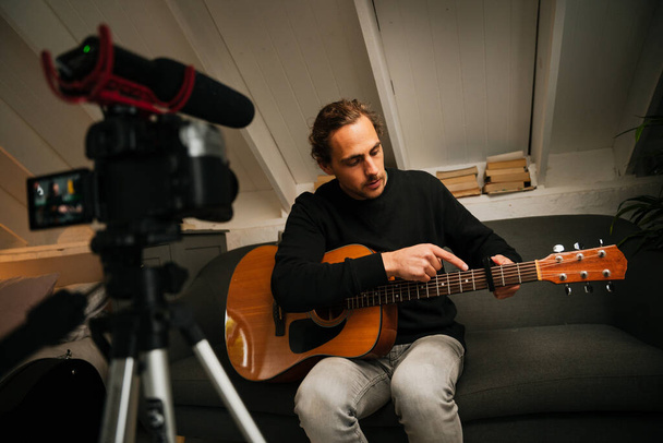 Młody kreatywny mężczyzna uczy i edukuje lekcje gry na gitarze online, vlogging i produkcji wideo - Zdjęcie, obraz