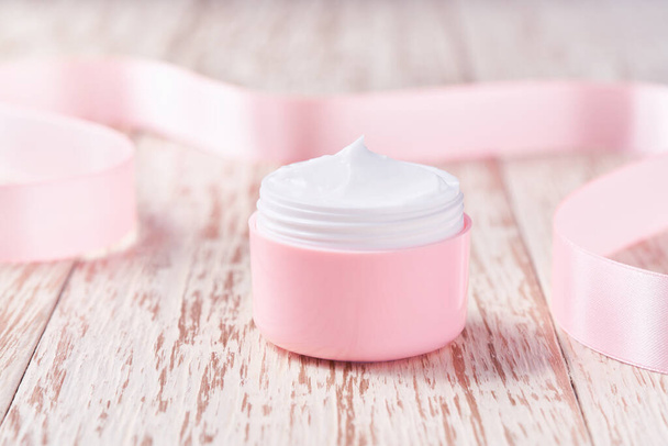 Natural moisturizer cream or body lotion cosmetic series of premium moisturizing and nourishing cosmetics. Plastic pink jars of night cosmetics on a wooden table. - Foto, Imagen