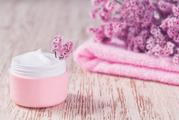 Creme cosmético de ervas curativas, produto higiênico para a pele ou máscara de maquiagem relaxante em um frasco rosa com uma toalha em uma mesa de madeira. - Foto, Imagem