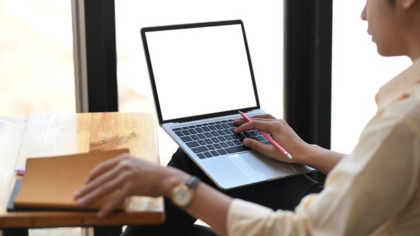 Image recadrée d'un homme intelligent travaillant avec un ordinateur portable blanc à écran blanc assis au bureau de travail en bois sur un bureau moderne en arrière-plan. - Photo, image