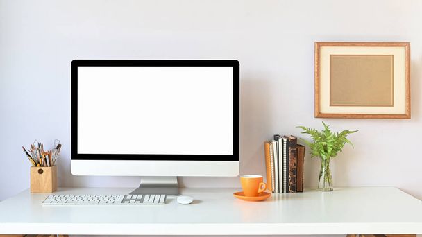 Monitor del computer di spazio di lavoro che mette sulla scrivania bianca insieme con roba dell'ufficio sopra la parete bianca ordinata del salotto come sfondo. - Foto, immagini