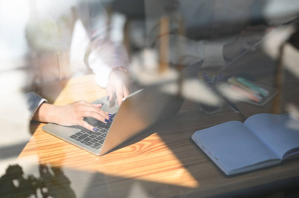 Обрезанное изображение через окно бизнес-команды, работающей с ноутбуком, сидя вместе за деревянным рабочим столом. - Фото, изображение