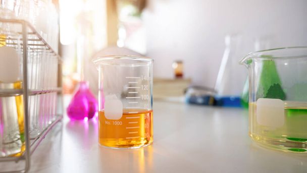 Foto de equipamentos científicos e produtos químicos de vidro reunidos na mesa de trabalho branca sobre a parede branca do laboratório como fundo. - Foto, Imagem