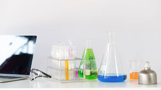 研究室の白い壁の上の白い作業机の上に背景として一緒に置く科学機器、化学ガラス製品やコンピュータのラップトップの写真. - 写真・画像