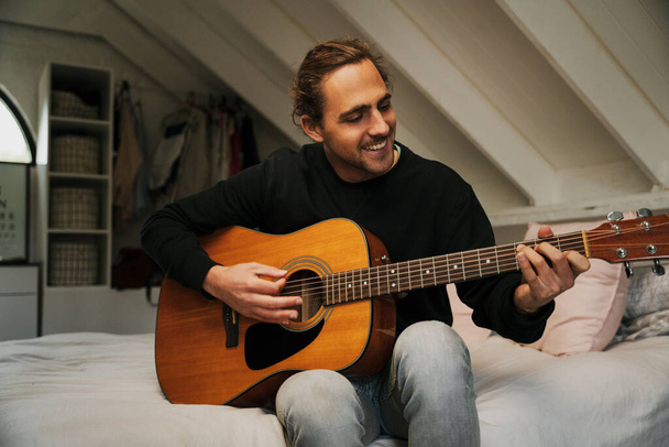 Кавказький музикант грає на гітарі у зручній спальні. - Фото, зображення