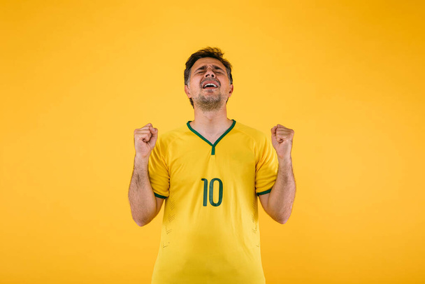 黄色のジャージーでブラジルのサッカーファンは彼の拳をきれいにし、彼のチームのために応援yells. - 写真・画像