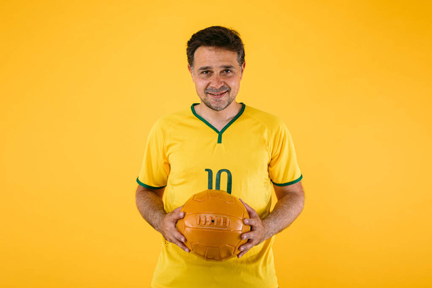 Fußballfan mit gelbem Trikot und Retro-Ball in der Hand - Foto, Bild