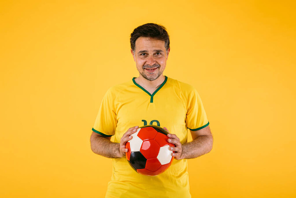 Braziliaanse voetbalfan met gele trui en een retro bal in zijn handen - Foto, afbeelding