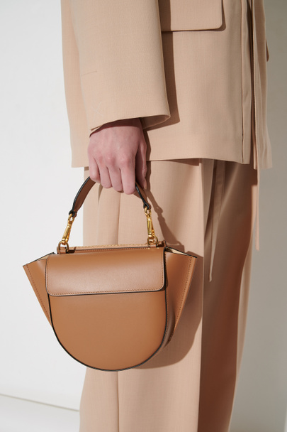 Kızın elinde kahverengi deri bir çanta. Klasik bej takım elbiseli, lüks çantalı biri. Dikey fotoğraf. - Fotoğraf, Görsel