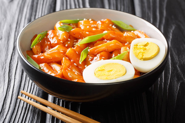 Корейская уличная еда Tteokbokki или dukbokki, приготовленная в остром соусе, подается с вареными яйцами и зеленым луком крупным планом в миске на столе. hhhonta - Фото, изображение