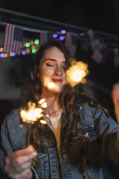 A young Spanish female holding Bengal sparklers and enjoying the moment with closed eyes - Photo, image