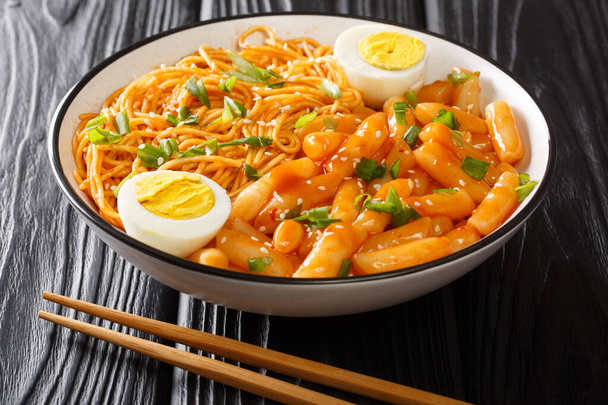 Rabokki vagy Ramyeon és Tteokbokki kombinációja zöldhagymával és főtt tojással keverve. Koreai fűszeres kaja közelkép egy tálban az asztalon. horizont - Fotó, kép