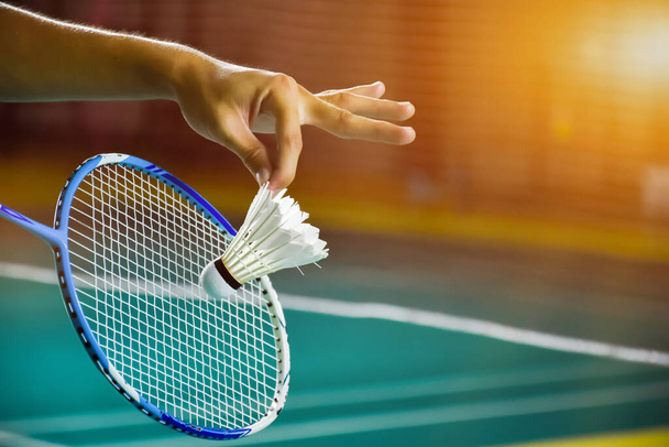 Badminton raketi ve eski beyaz mekikçik oyuncunun elinde tutarken ilerideki ağda servis yaparken, bulanık badminton sahası geçmişi ve seçici odaklanma. - Fotoğraf, Görsel