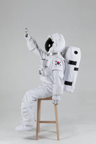 Astronaut sitting on a wooden chair, white background - Fotoğraf, Görsel