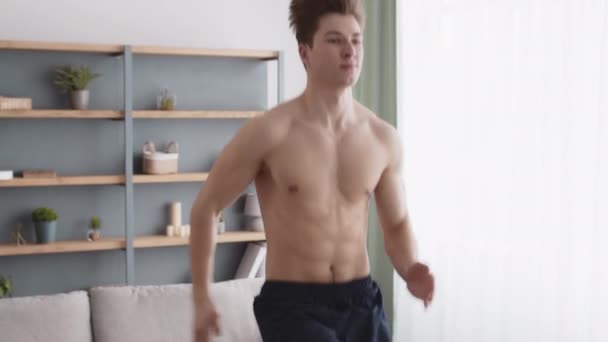 Primer plano retrato del hombre activo velocista corriendo en el lugar, haciendo ejercicio en casa con el torso muscular desnudo, seguimiento de disparo - Metraje, vídeo