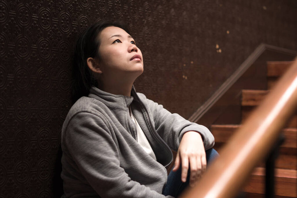 young beautiful Asian woman in pain suffering depression - dramatic indoors portrait on staircase of sad and depressed Chinese girl as victim of bullying and abuse  - Zdjęcie, obraz