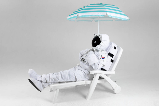 astronaut resting under parasol, white background - Foto, afbeelding