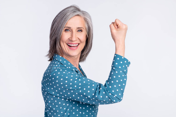 Profile portrait of cheerful astonished aged woman fist up toothy smile celebrate isolated on grey color background - 写真・画像