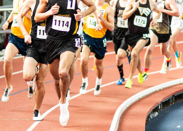 Een grote groep van middelbare school mannelijke lopers racen de mijl op een indoor track. - Foto, afbeelding