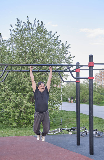 Vanhempi aasialainen mies treenaa puistossa urheilukentällä kaupunkikuvaa vasten.. - Valokuva, kuva