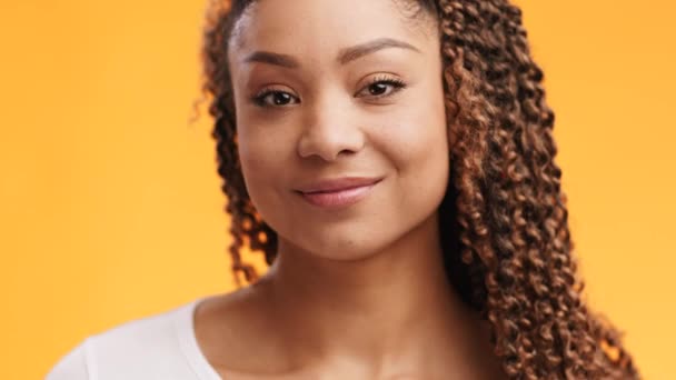 Közelkép portré játékos afro-amerikai hölgy kacsint és mosolyog a kamera, narancs stúdió háttér, lassított felvétel - Felvétel, videó