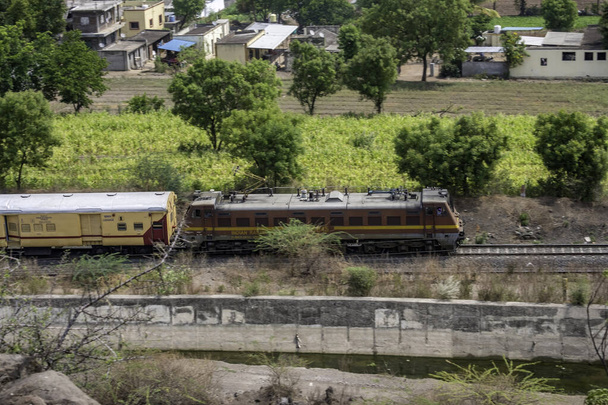 Matkustajajuna, jota vetää sähköinen loco keskellä vihreää ympäristöä Urulissa lähellä Pune Intiaa. - Valokuva, kuva