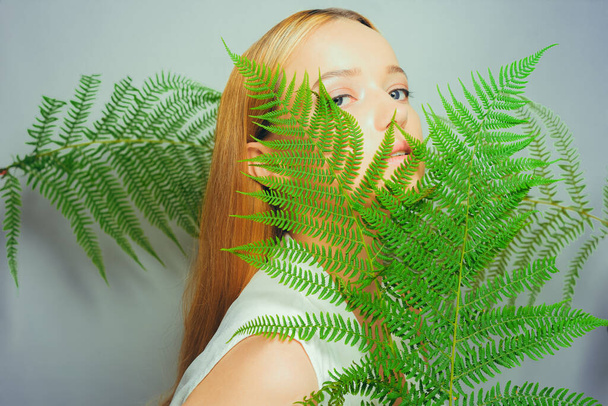 Piękna młoda blondynka z doskonałą skórę i naturalny makijaż pozowanie przed rośliną tropikalnych zielonych liści tła. nastolatek model włosy pielęgnacja z jej twarz moda. - Zdjęcie, obraz