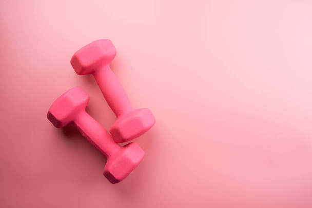 Two pink female dumbbells isolated on pink background close-up with copy space. Fitness concept, weight loss and sport activity, top view, flat lay - Foto, imagen