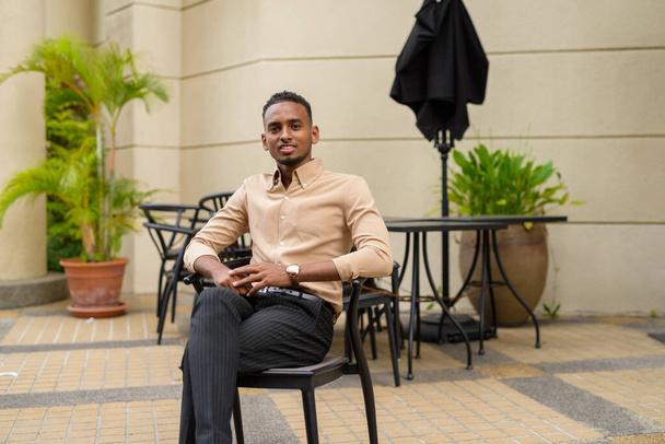 Portrait of handsome black young African businessman wearing casual clothes outdoors in city - Photo, Image
