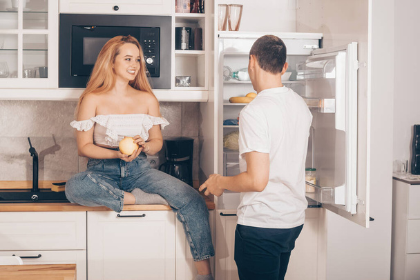 The guy and the girl in the kitchen. Loving couple at home. The man feeds and gives the woman an apple. The couple eats healthy food. Useful ration. Prepare breakfast together, morning. - Valokuva, kuva