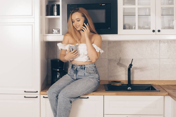Food delivery, mobile shops, online shopping. A woman at home in the kitchen at the will of the refrigerator. A girl with a good figure holds a mobile phone in her hands - Foto, Bild