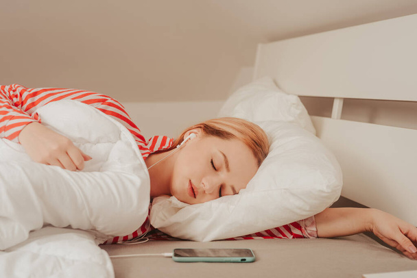 赤い縞模様のパジャマを着た白いベッドの上の美しい女の子が寝ている。健康な睡眠。ベッドの上で目を閉じて長い経髪の女性. - 写真・画像