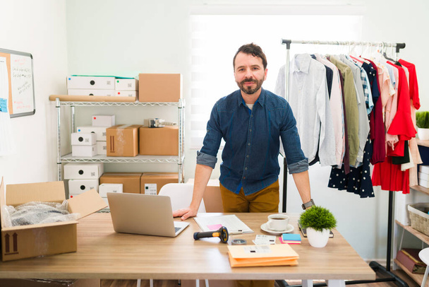 Hispanic young entrepreneur behind his office desk and working on making packages with fashion clothes to ship to their customers  - Foto, Imagen
