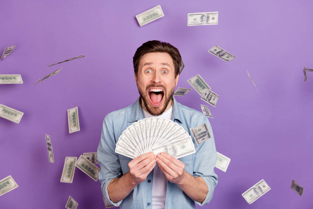 Photo of happy cheerful crazy young man hold money cash fall fly lottery shock isolated on purple color background - Fotó, kép