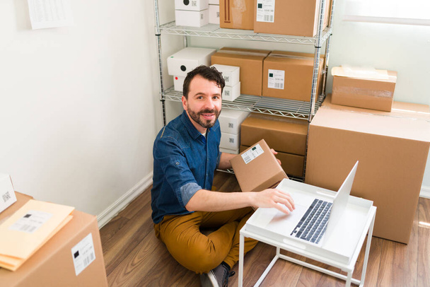 Portrait of a handsome hispanic man smiling and making eye contact while preparing to ship packages for his customers' orders - Photo, image