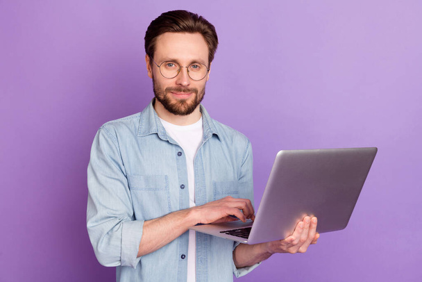 Photo of serious young man hold computer good mood wear glasses isolated on purple color background - Fotó, kép