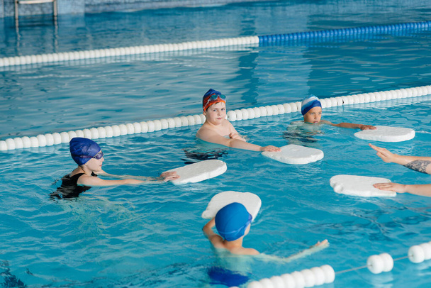Um grupo de meninos e meninas treinam e aprendem a nadar na piscina com um instrutor. Desenvolvimento de esportes infantis. - Foto, Imagem