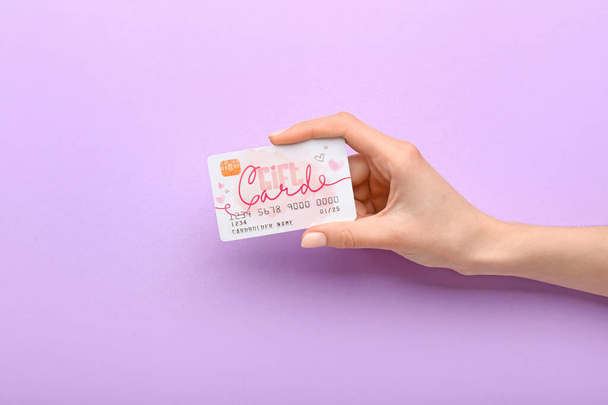 Female hand and gift card on color background - Foto, imagen