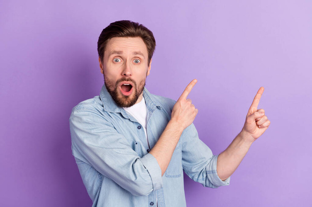 Photo of young shocked amazed surprised man point fingers copyspace advertisement isolated on purple color background - Фото, изображение